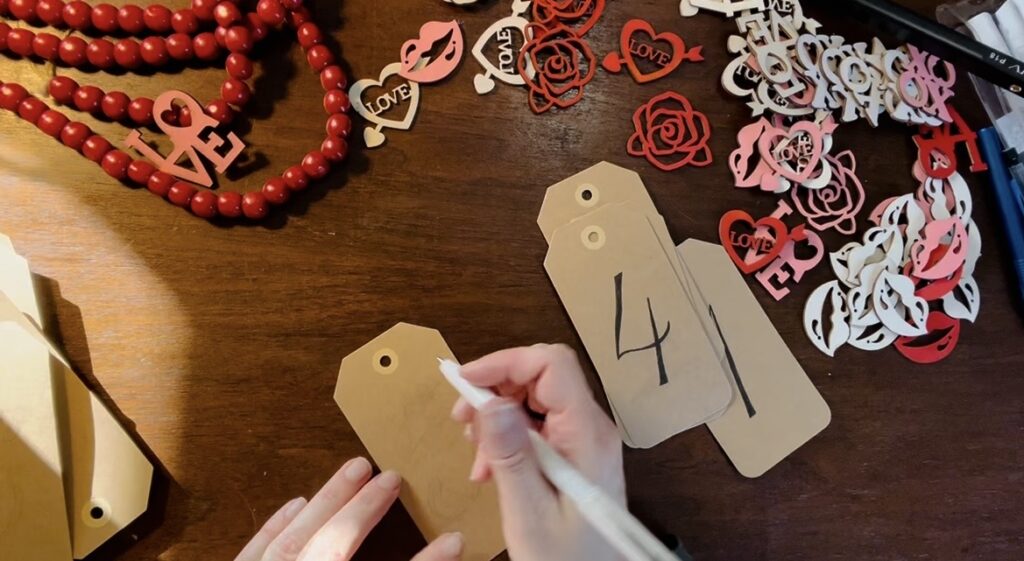 Hand writing out numbers on brown craft tags for valentine love notes