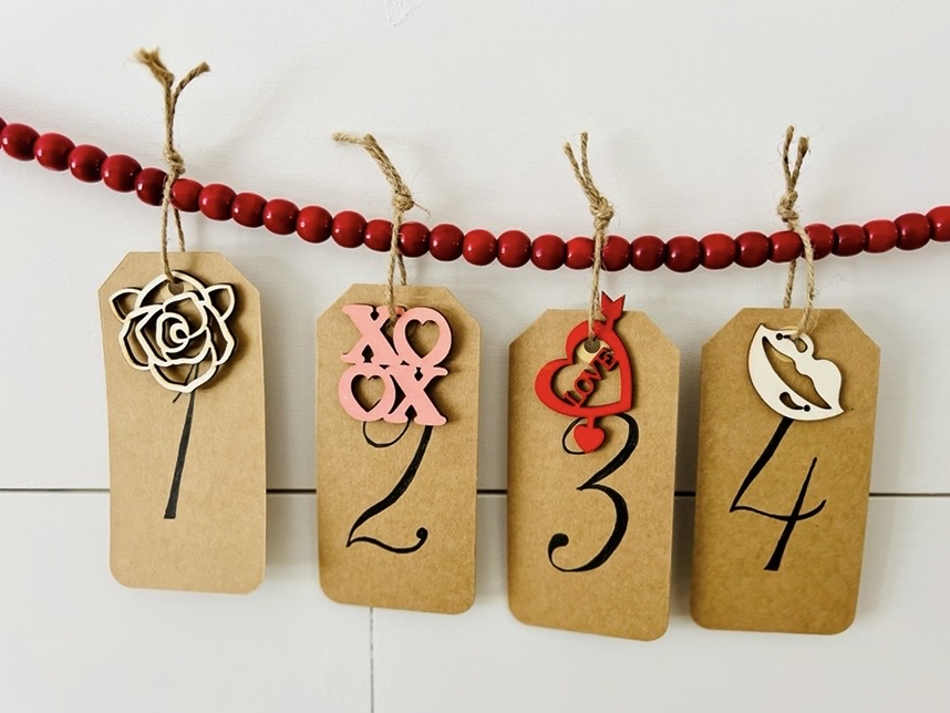 1-4 Craft Brown tags numbered with valentine wooden cutouts hanging on red beads on shiplap wall
