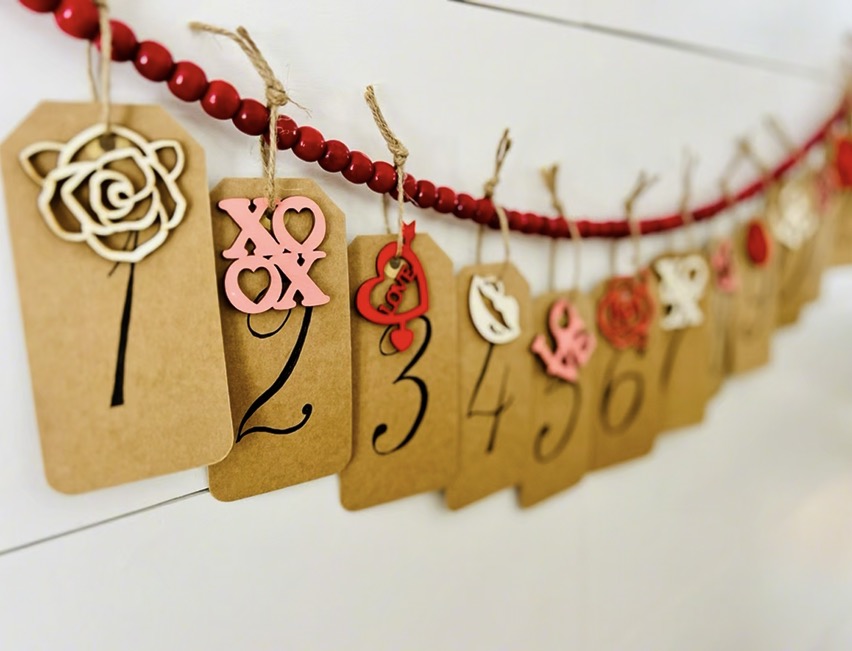 Numbered Valentine craft gift tags with wooden valentine decorations hanging on red beads on shiplap wall