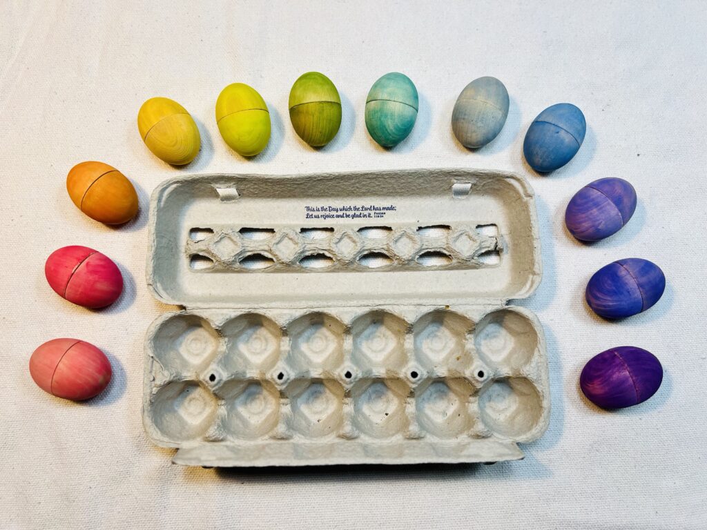 Array of colorful wooden eggs around egg carton box